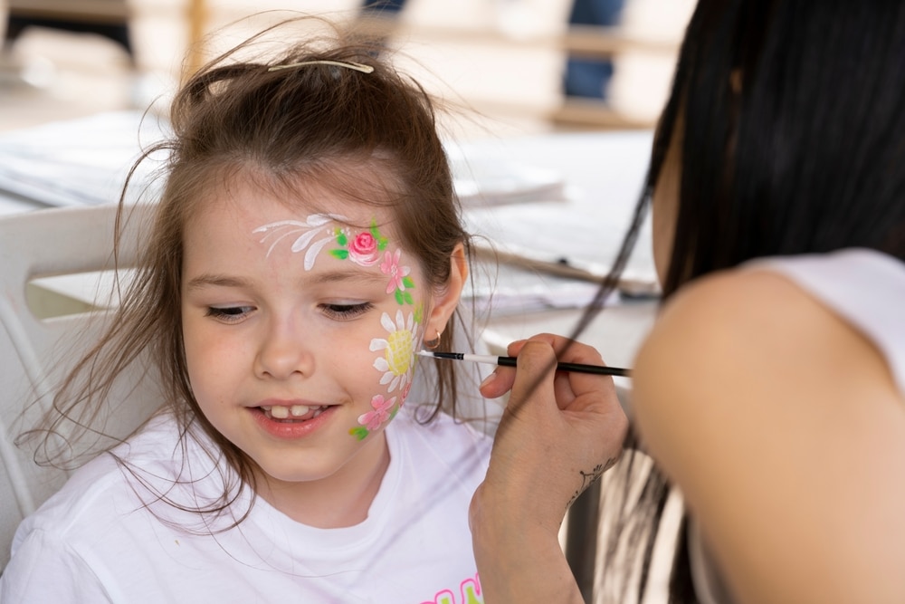 A view of a a girl applying face paint over a little girl's face