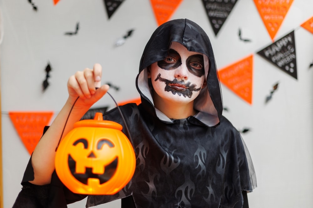 A view of a girl holding pumpkin with skull face paint on