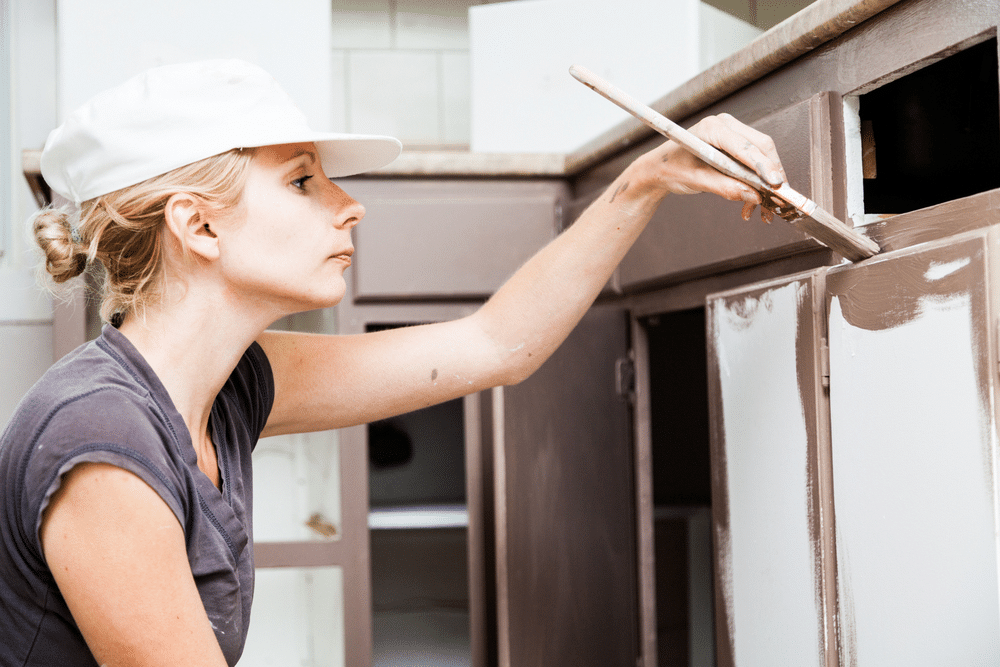 A view of a lady painting a kitchen cabinet