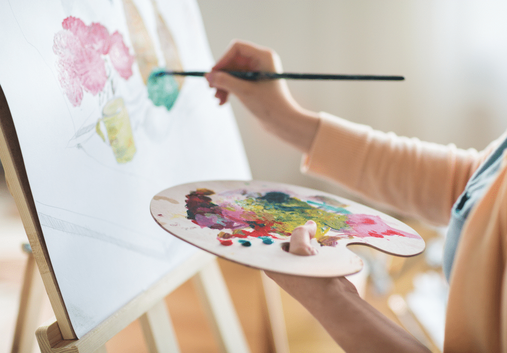 A view of a person holding a palette and paintbrush to the canvas