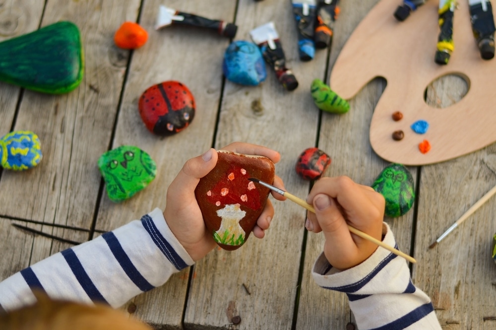 An overhead view of little hands painting a rock