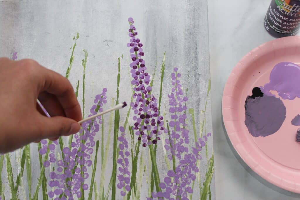 A hand holding a cotton swab over a Lavender Painting