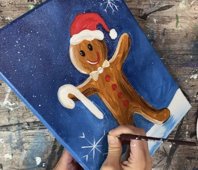 A person drawing on a gingerbread man painting