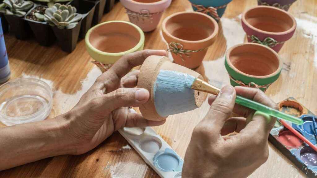 A person painting the pots with a paintbrush