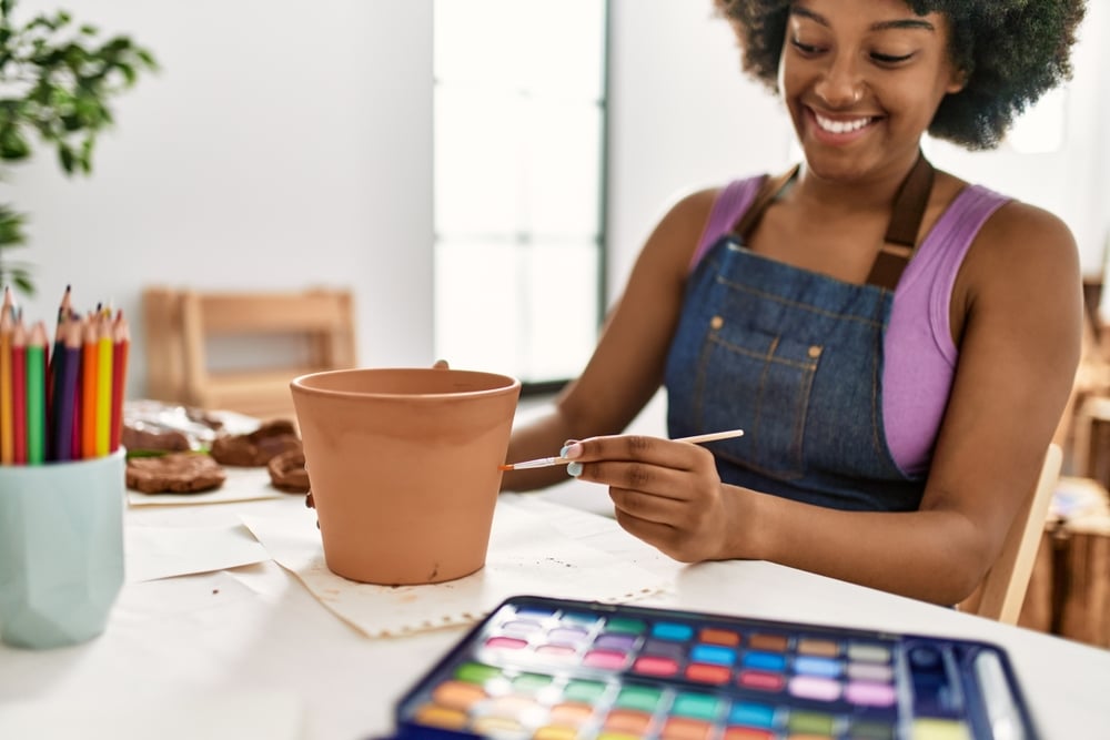 A view of a girl painting a pot with a brush