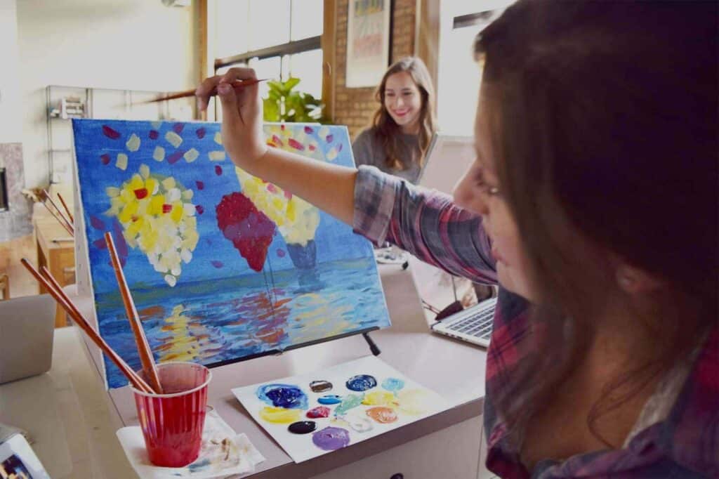 A woman holding a paint brush to teach painting on a canvas