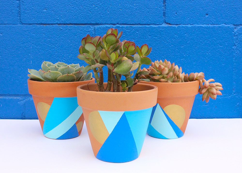 Three blue painted pots with geometric shapes on them against a blue painted wall