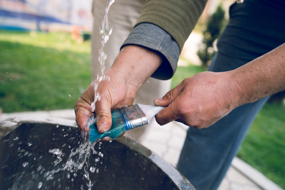 Close up on hands of a craftsman washing a brush cleaning after the painting work finished job