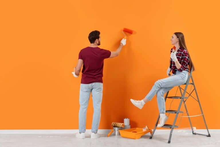 Man Painting Orange Wall And Woman Sitting On Folding Ladder