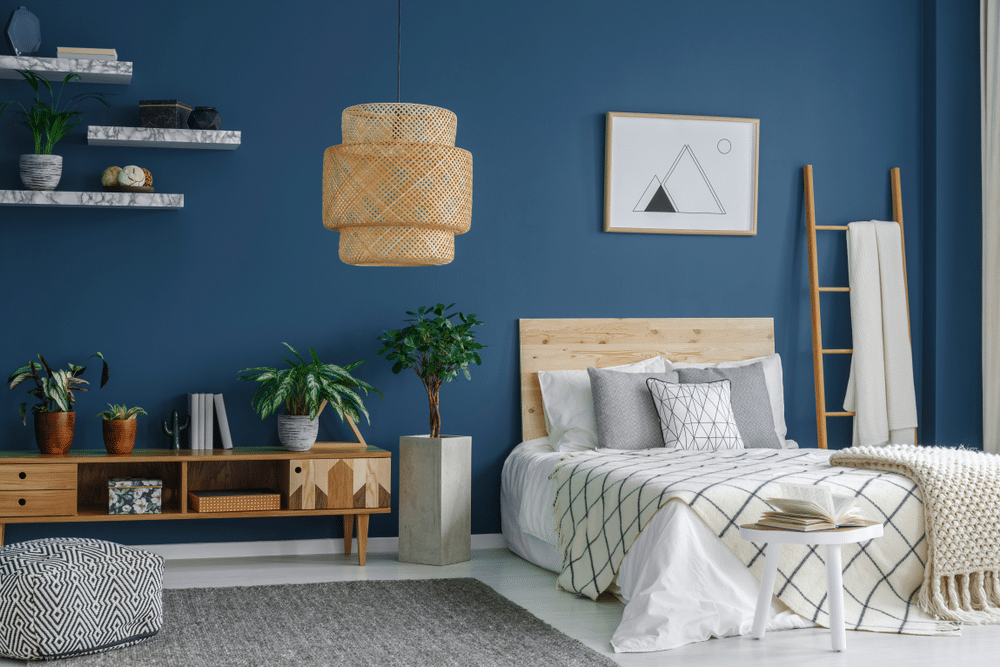 Side view of a blue bedroom interior with a modern lamp double bed plants and cabinet