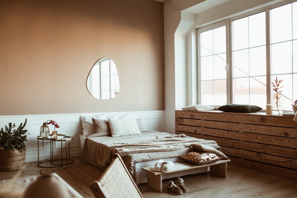 Stylish beige color bedroom with bed linen pillows mirror bedside table with red berries bouquet furniture