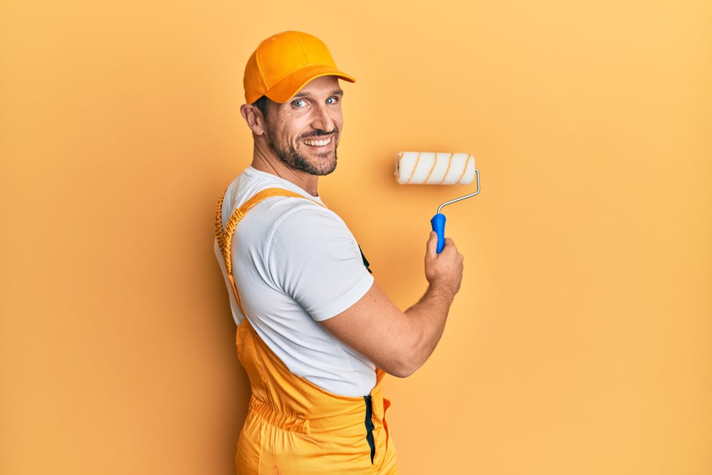 Young Caucasian Painter Smiling Happy Painting Wall Using Roller