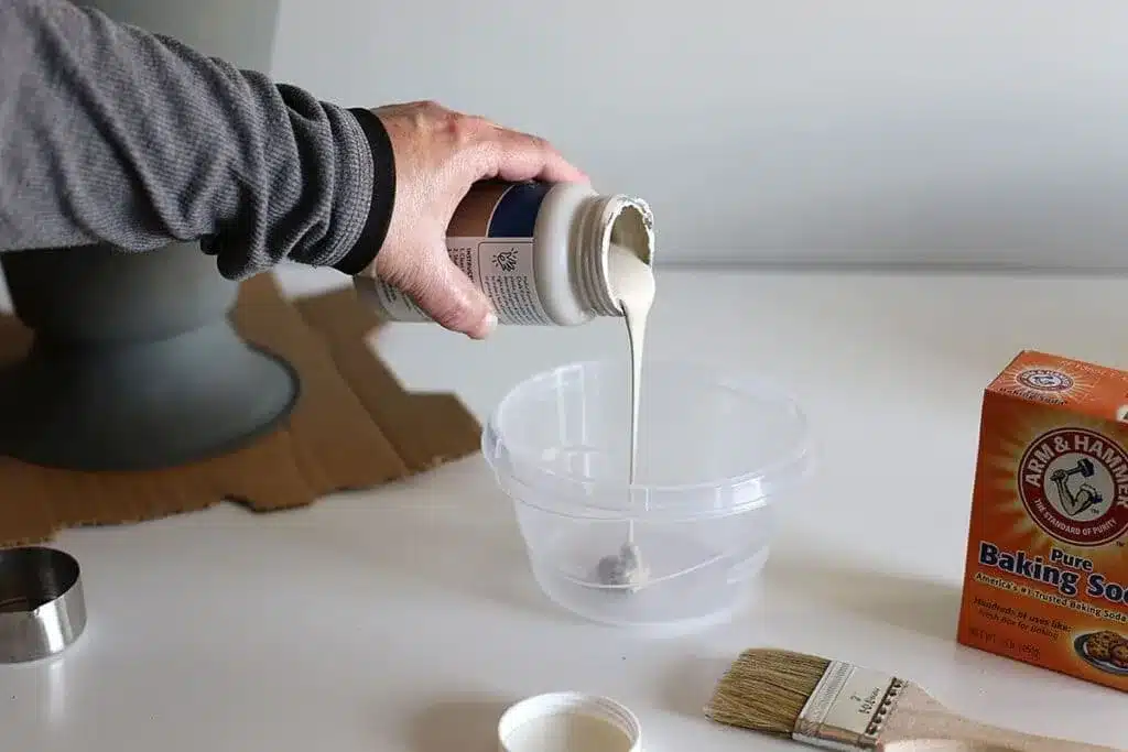 a man pouring latex paint in a bowl along with a box of baking soda and a paint brush