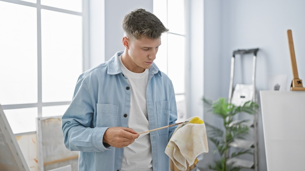 Handsome Young Caucasian Man A Concentrated Artist Meticulously Cleaning Paintbrushes