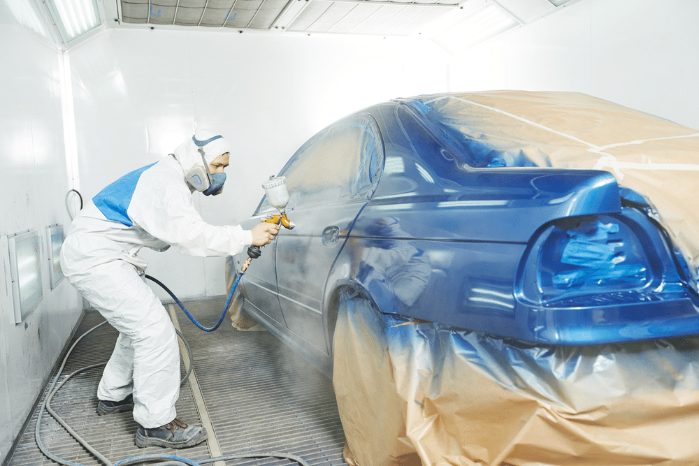 automobile repairman painter in protective workwear painting the car