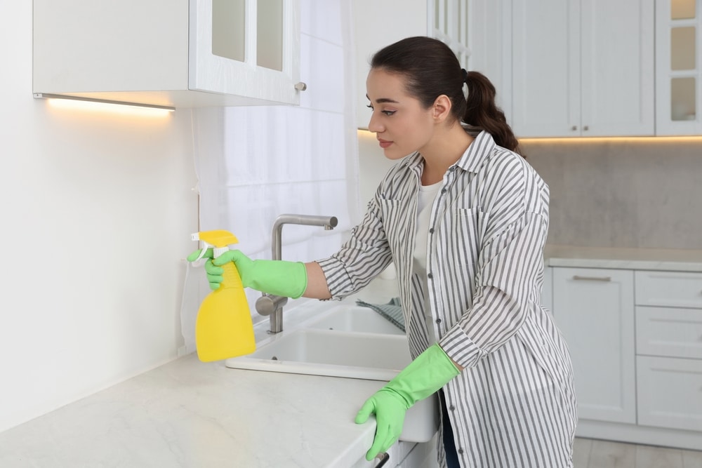 Woman With Spray Bottle Cleaning Wall In Kitchen