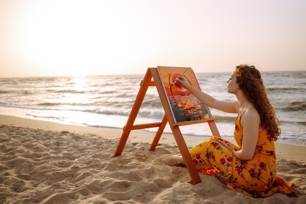 A view of a woman sitting on the beach painting