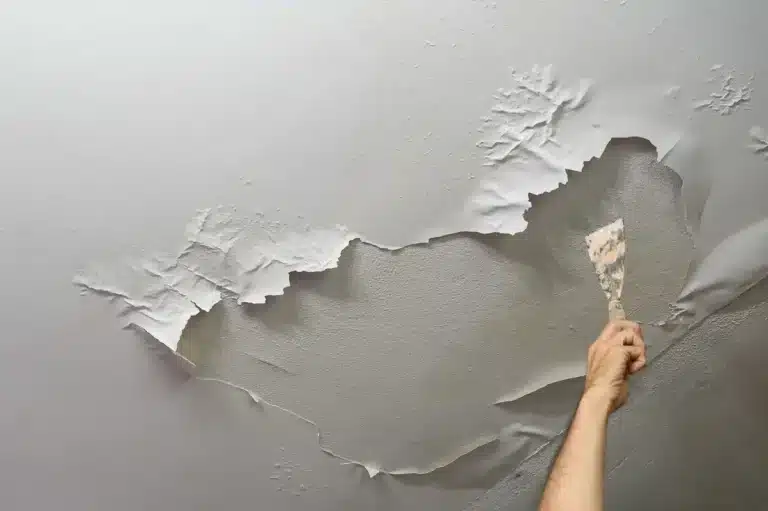 view of a hand trying to fix bubbling paint on wall