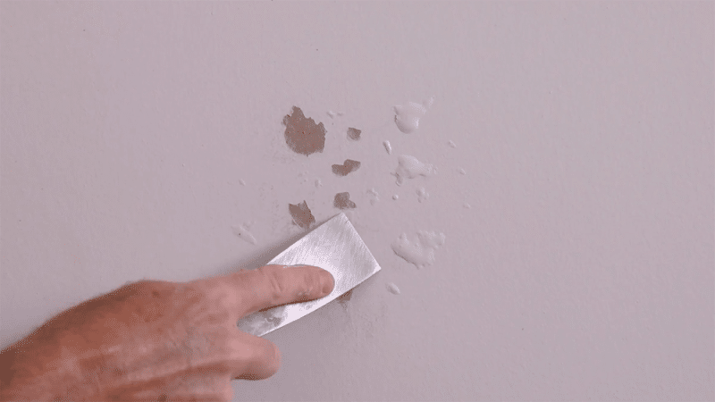 zoomed view of a hand scratching off bubbling paint