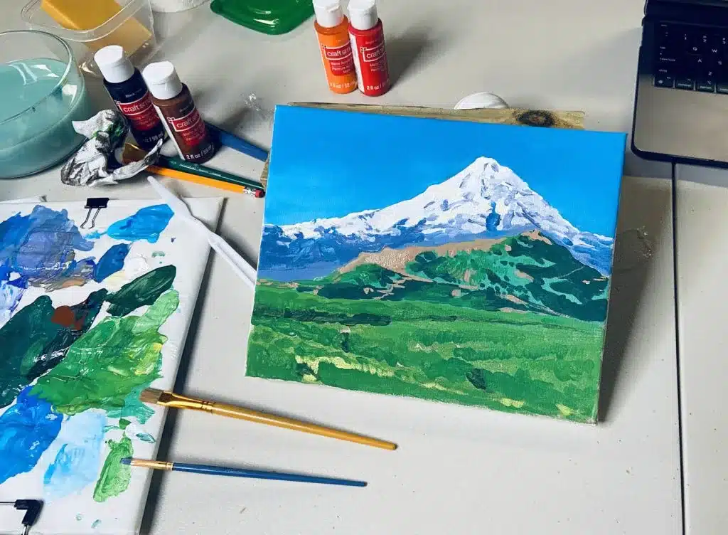 view of a scenic painting different colors on a board and few brushes scattered