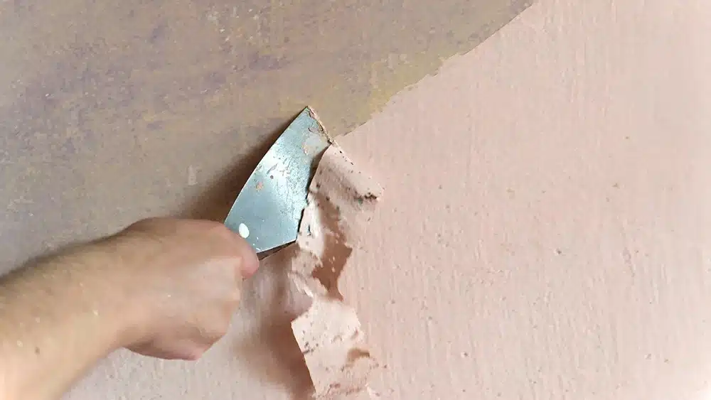Close up of a person scraping peeling paint from a wall with a putty knife