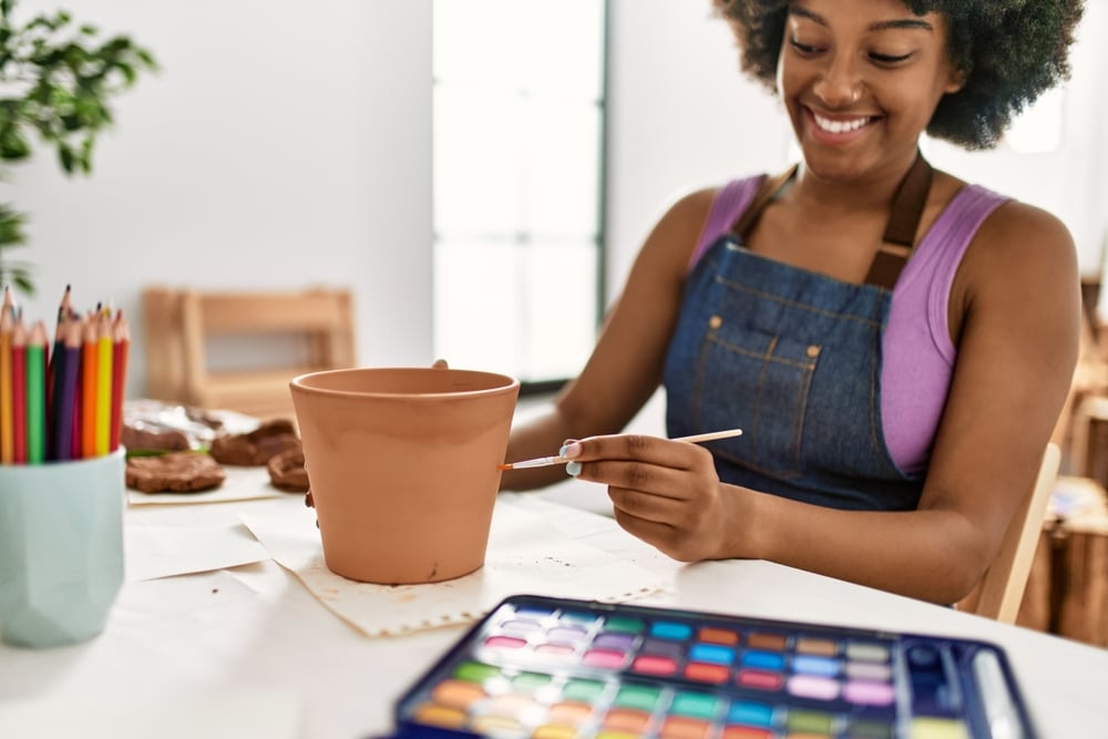 A view of a girl painting a pot with a brush