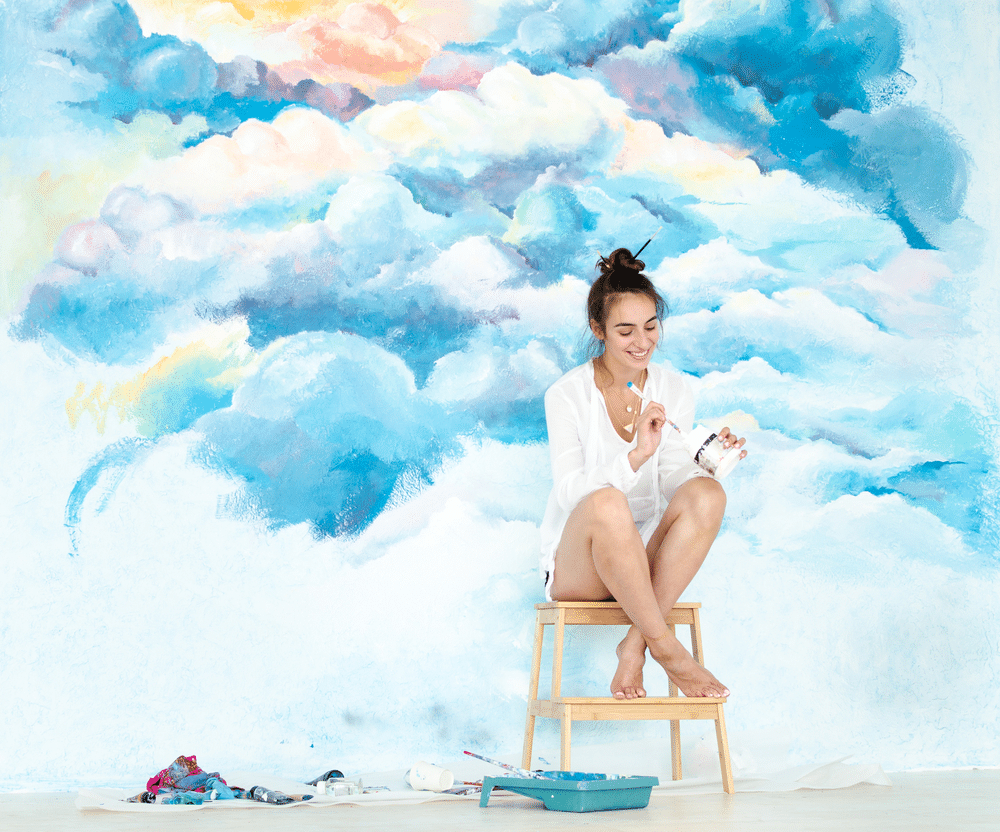 A view of a girl painting clouds on a wall A view of a girl painting clouds on a wall