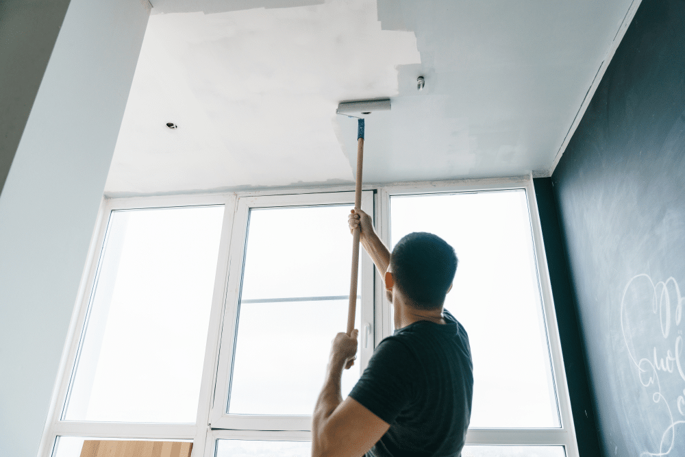 A view of a person using a ceiling roller brush for painting ceiling A view of a person using a ceiling roller brush for painting ceiling