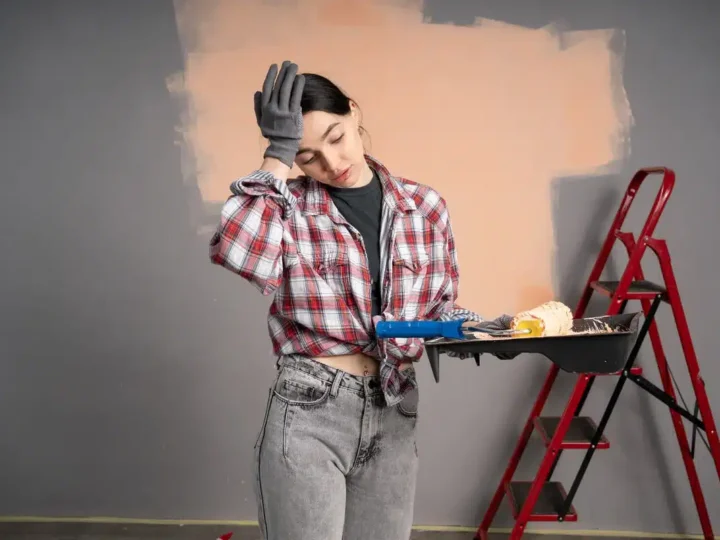a girl seems worried holding a paint roller a half painted wall on back