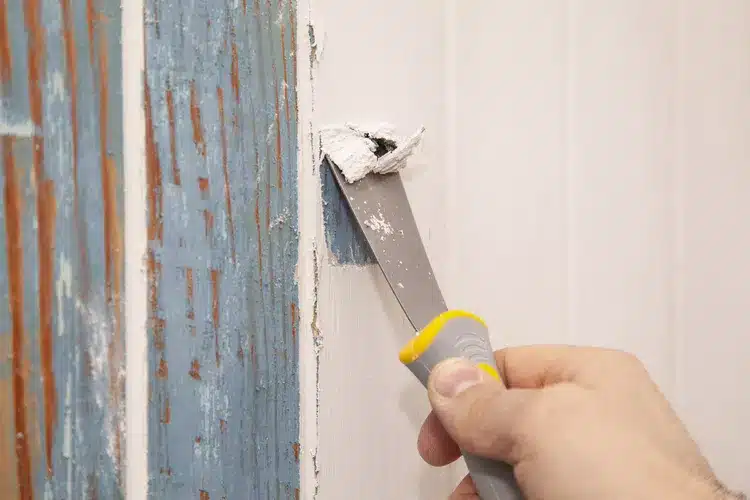 close up of hand holding a scraper and peeling the paint from wall close up of hand holding a scraper and peeling the paint from wall