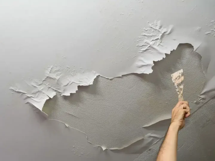 view of a hand trying to fix bubbling paint on wall